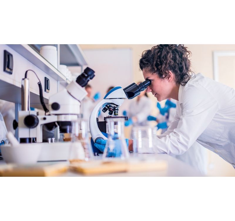 A woman is looking through a microscope in a laboratory.