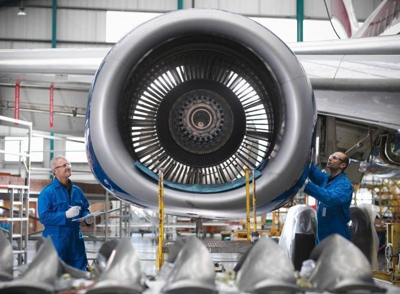 Two men are working on an airplane engine in a factory