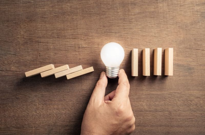 A person is holding a light bulb in front of a row of wooden blocks.