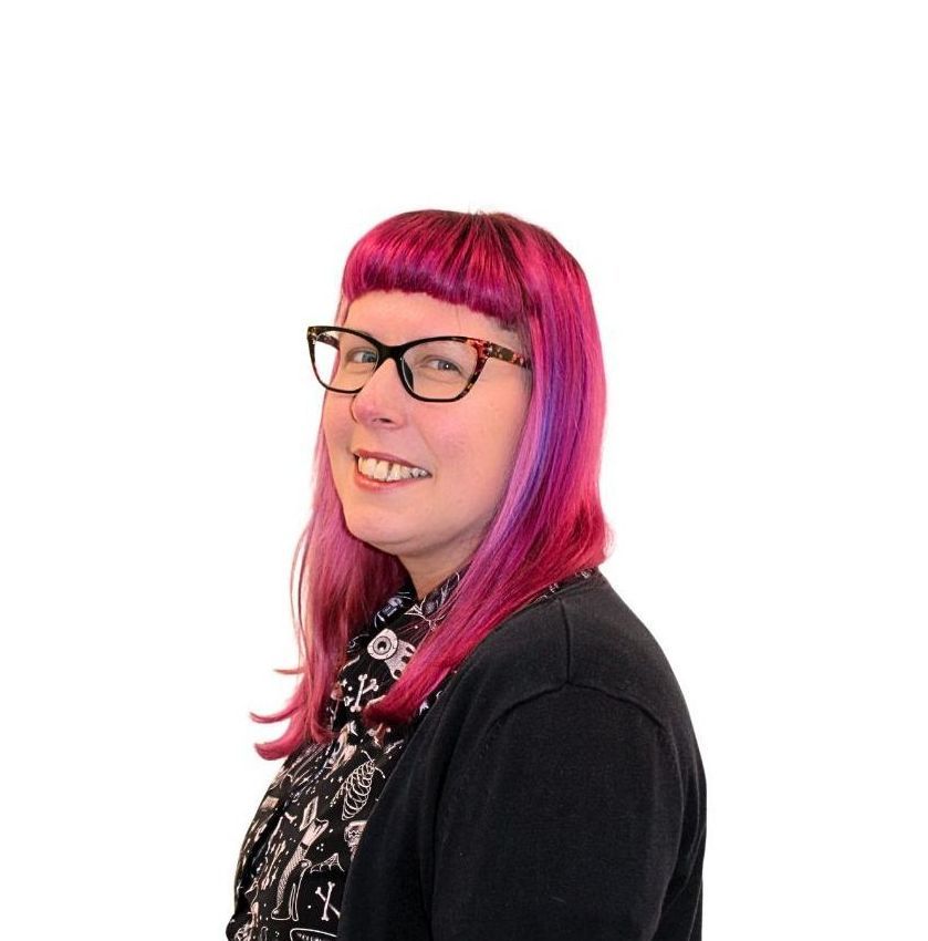 A woman with pink hair and glasses is smiling