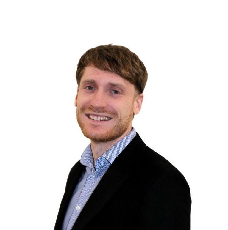 A man with a beard is wearing a black jacket and a blue shirt.