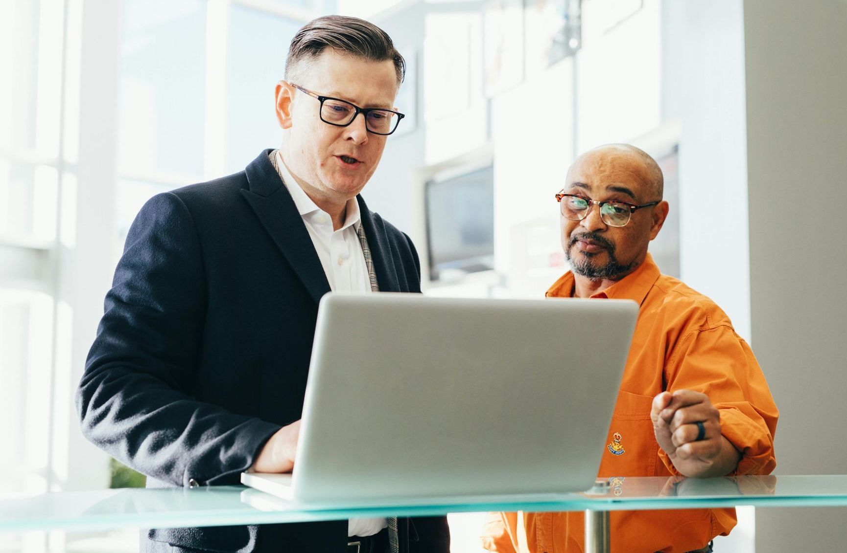 Two men are standing next to each other looking at a laptop computer.
