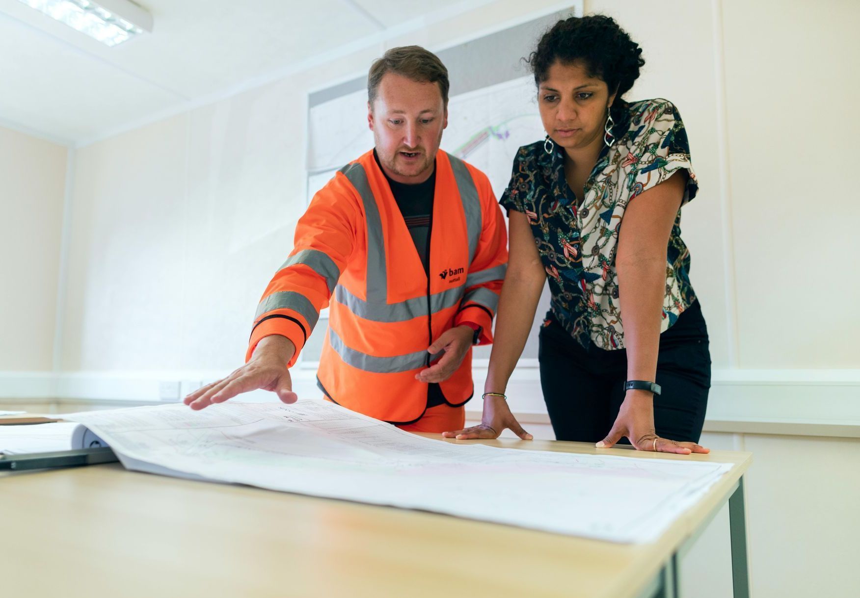 A man and a woman are looking at a blueprint on a table.