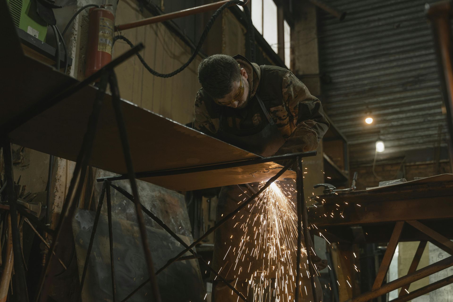 A man is cutting a piece of metal with a grinder in a factory.