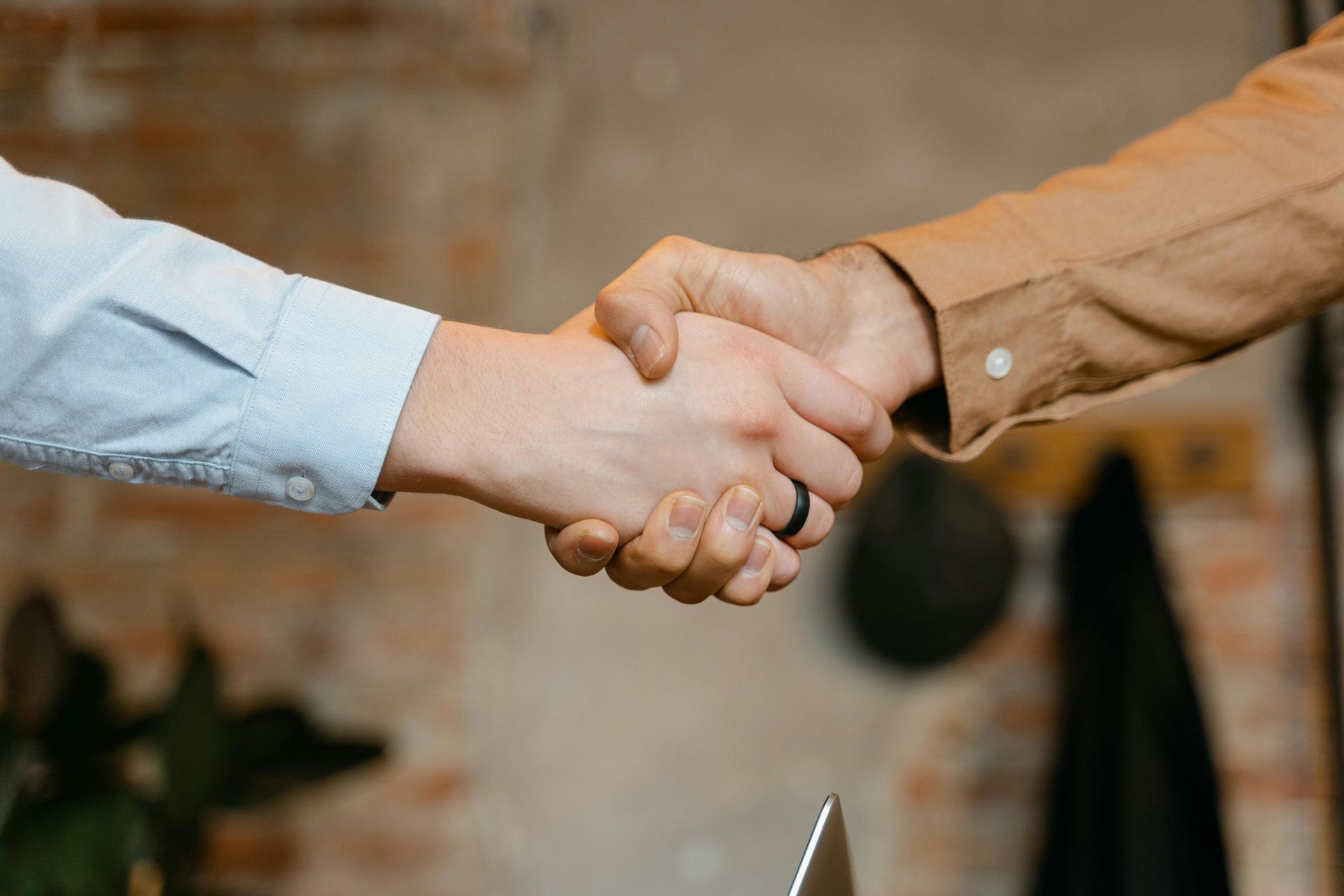 Two people are shaking hands in front of a brick wall.