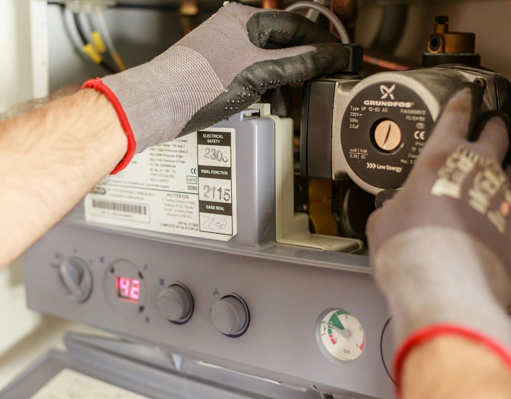 A person wearing gloves is working on a boiler.
