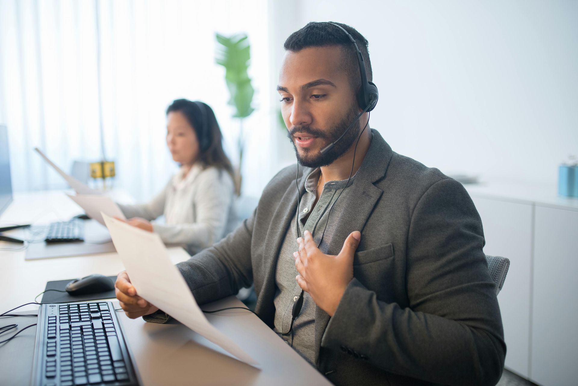 A man wearing a headset is sitting at a desk holding a piece of paper.