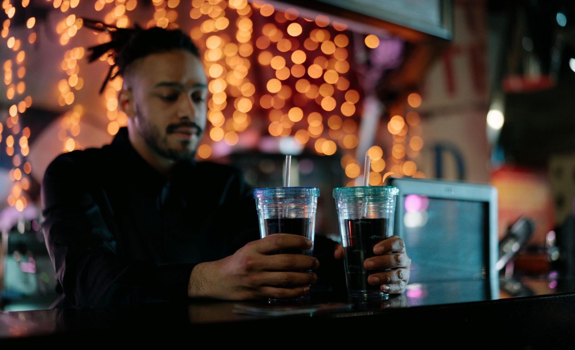 A man is sitting at a bar holding two cups of soda.