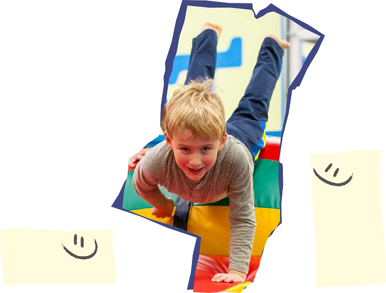Boy in gray shirt and blue jeans doing a handstand on a colorful mat.
