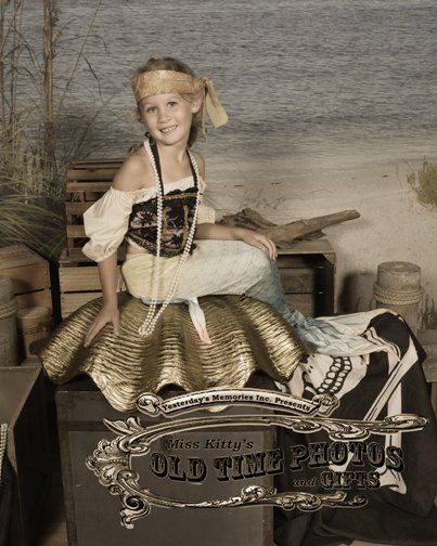 a little girl in a pirate costume is sitting on a trunk .