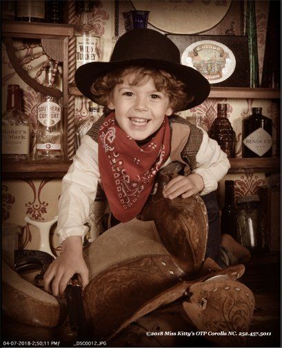 a young boy dressed as a cowboy is sitting on a saddle Miss Old Time Photos and Gifts    Corolla Outer Banks NC