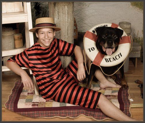a boy in a striped bathing suit sits next to a dog wearing a life preserver that says to beach