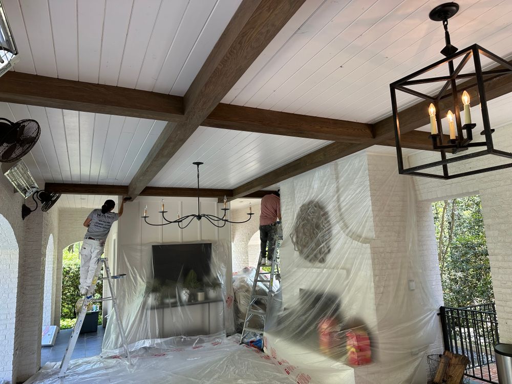 A man is standing on a ladder painting the ceiling of a room.