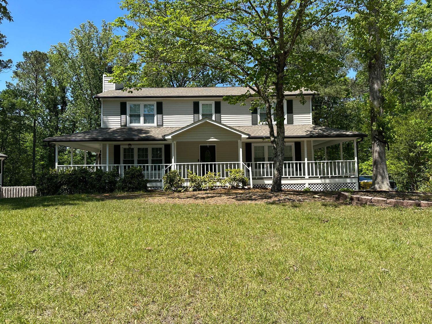 A large white house with a large porch is surrounded by trees and grass.