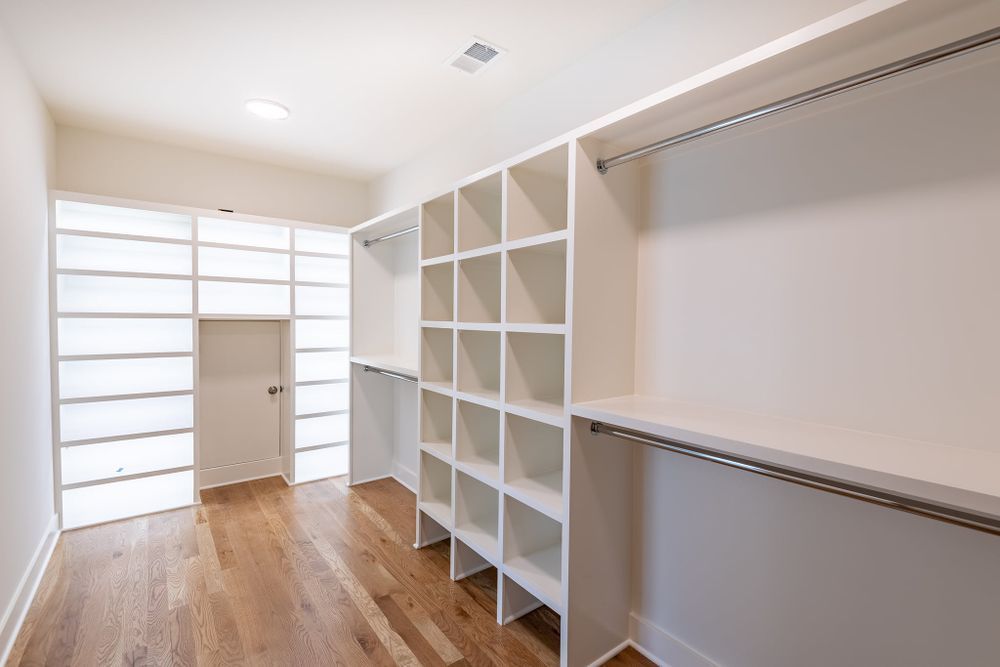 A walk in closet with hardwood floors and white shelves.