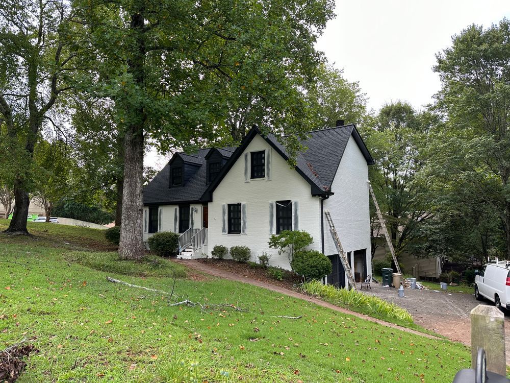 A white house with a black roof is sitting on top of a lush green hill.