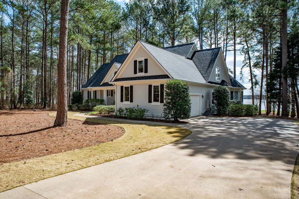 A white house with a black roof is surrounded by trees and a driveway.