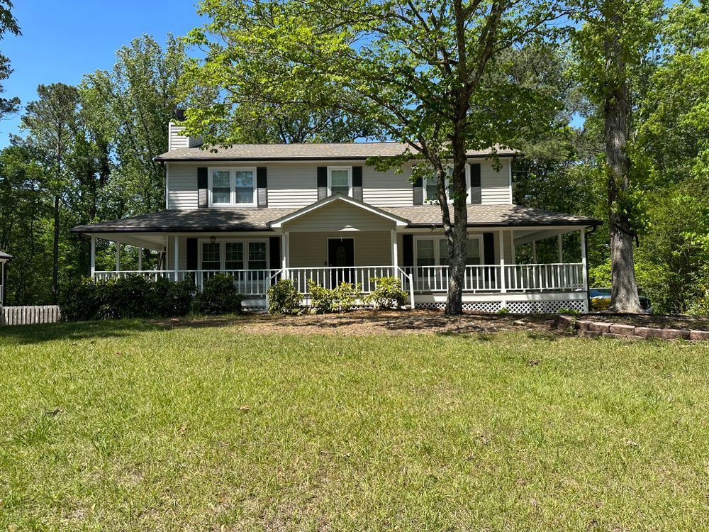 A large white house with a large porch is surrounded by trees and grass.