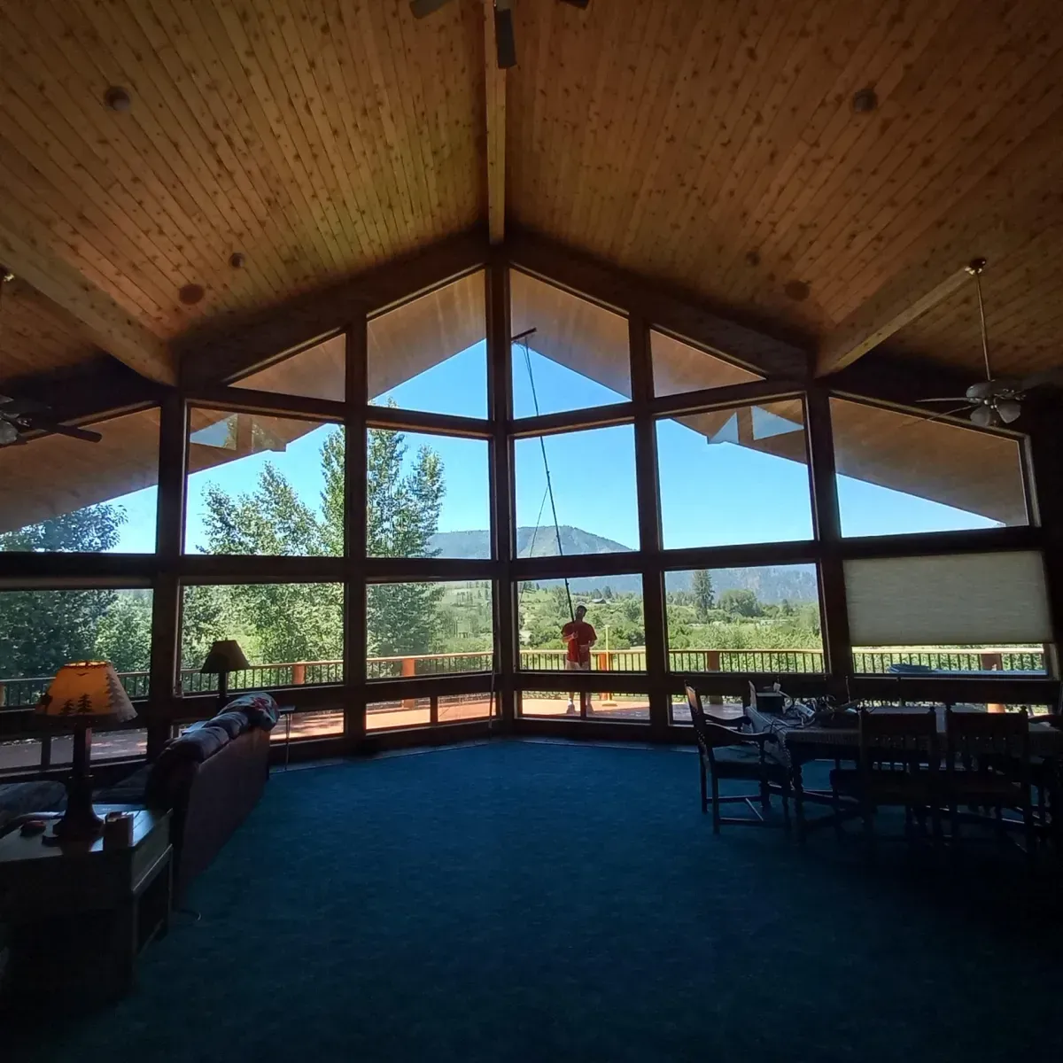 Interior of a lodge with large windows overlooking a mountain view; person standing outside.