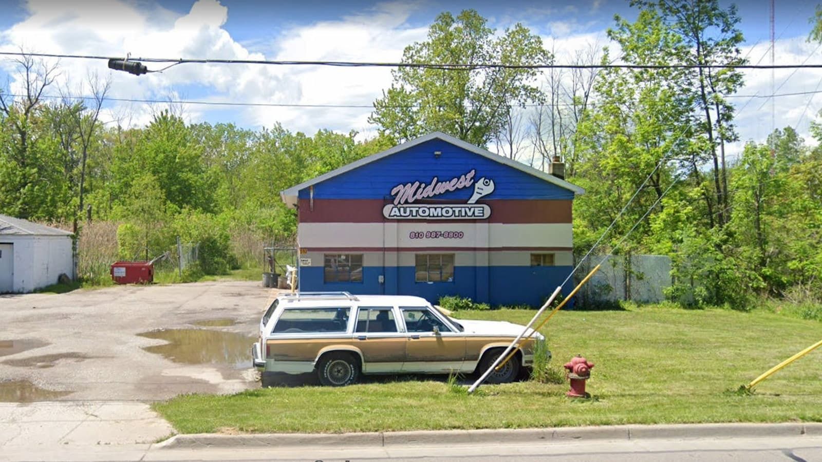 Midwest Jo’s Automotive building with a brown and white station wagon in front. Building has blue, white, and red stripes.