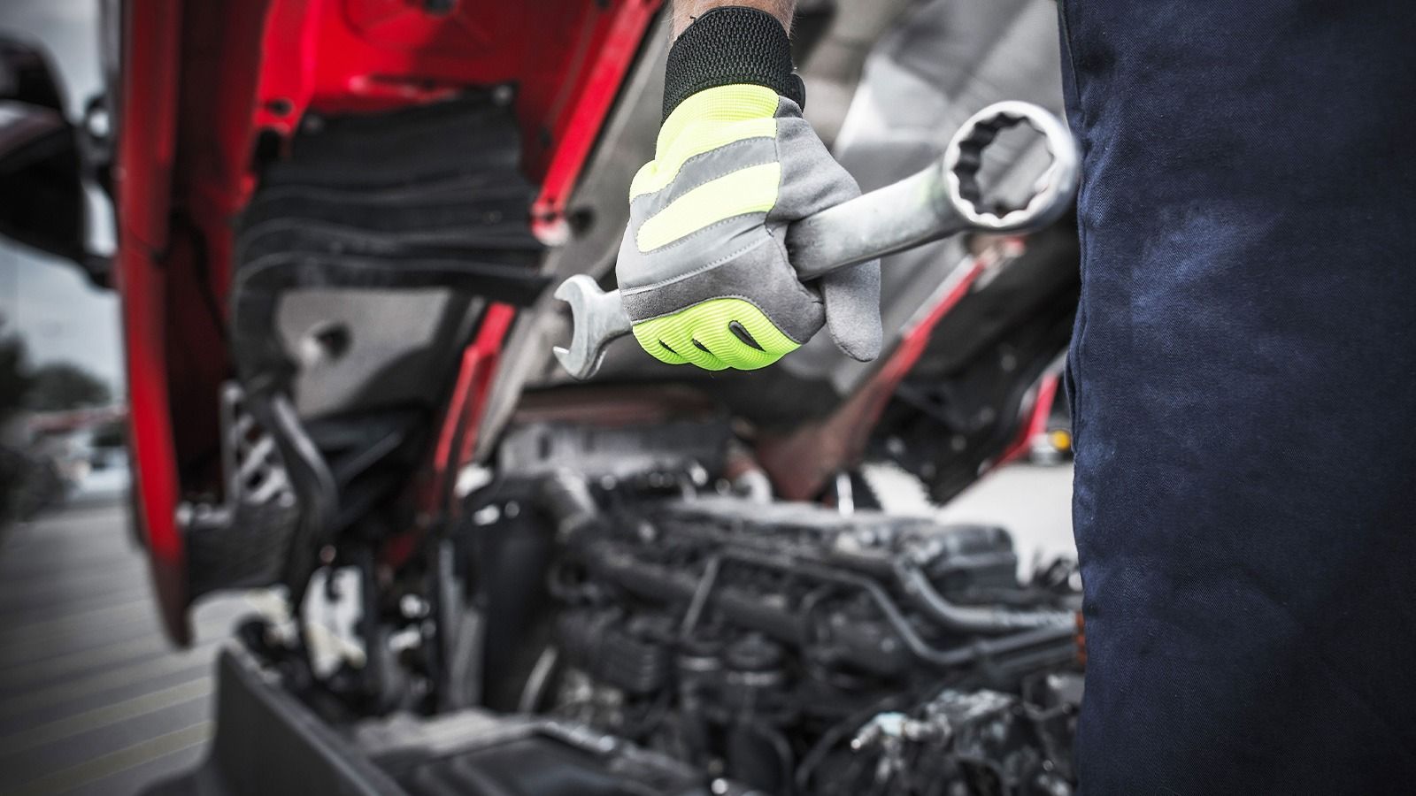 Mechanic with a wrench working on a red truck engine, wearing safety gloves.