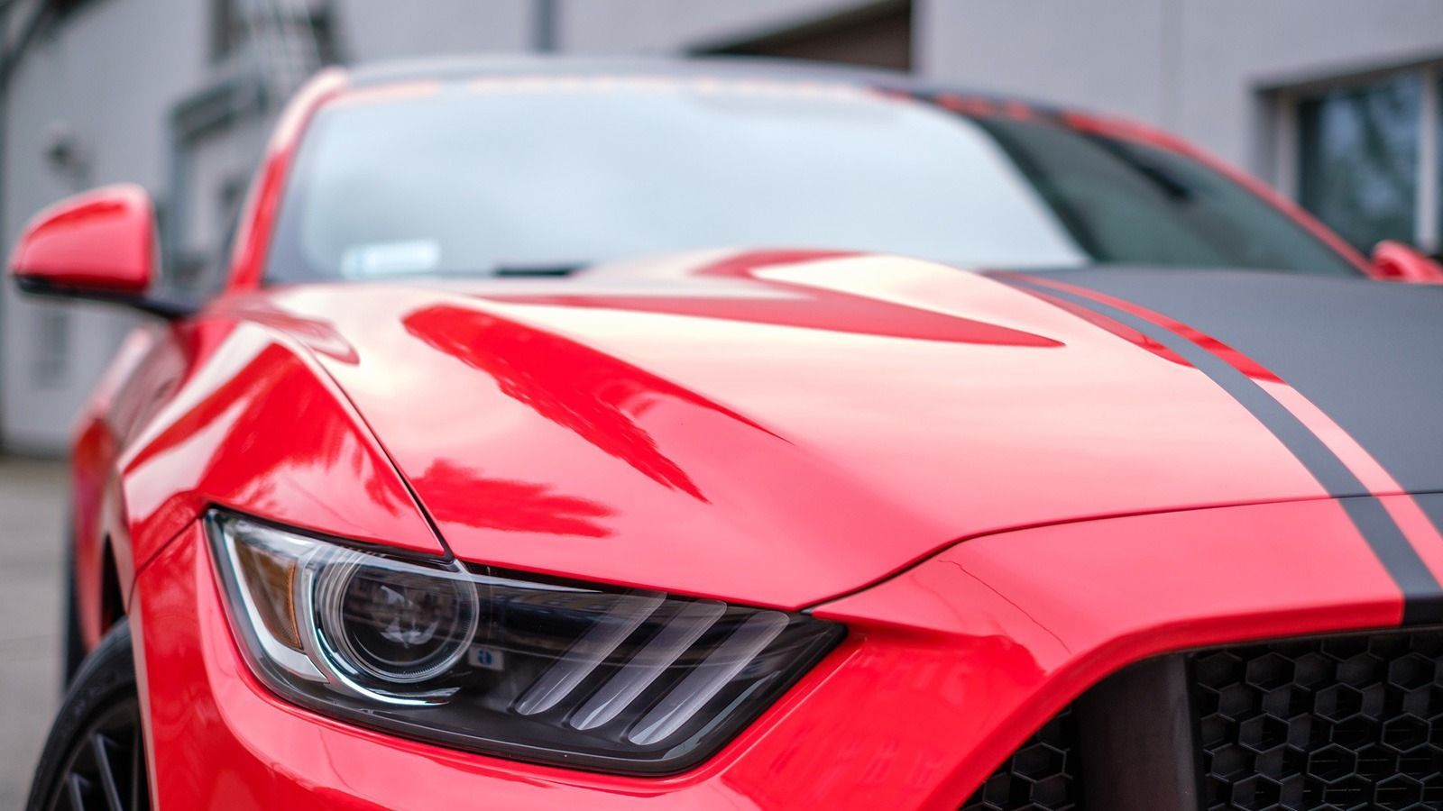 Red and black Ford Mustang car with black racing stripes on the hood.