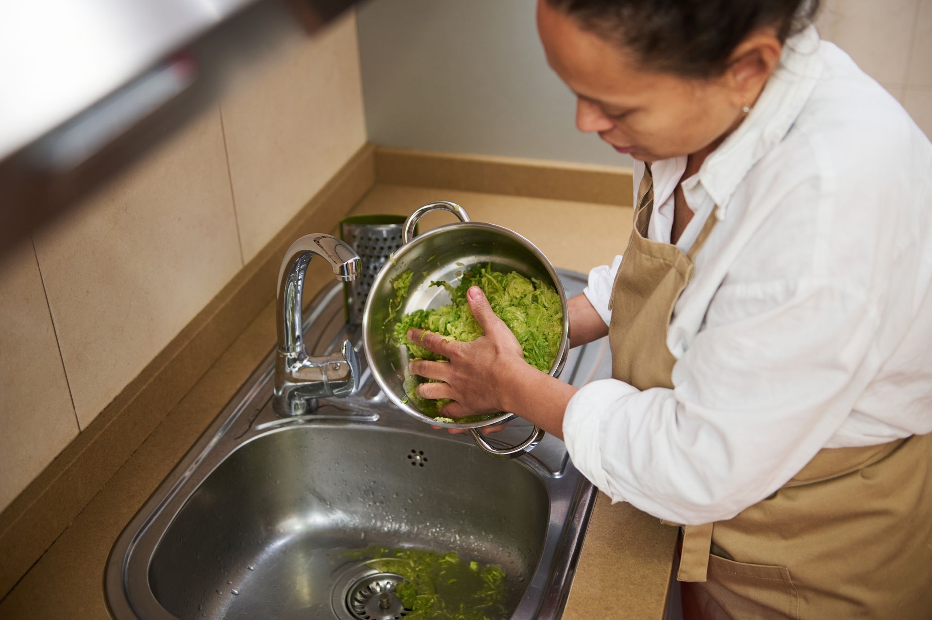 A woman is washing pots and pans in a kitchen sink.