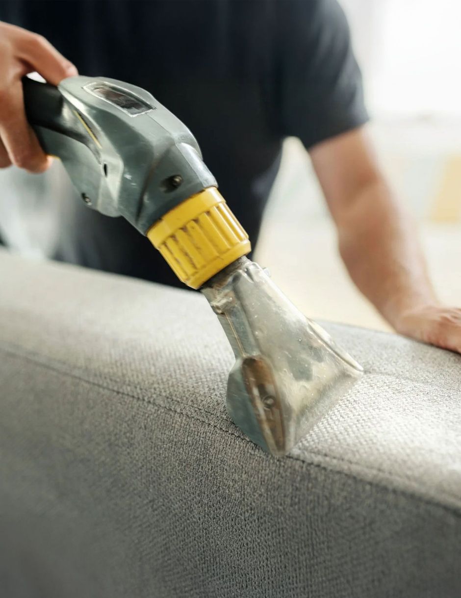 Hand using a carpet cleaning tool on a gray lounge upholstery
