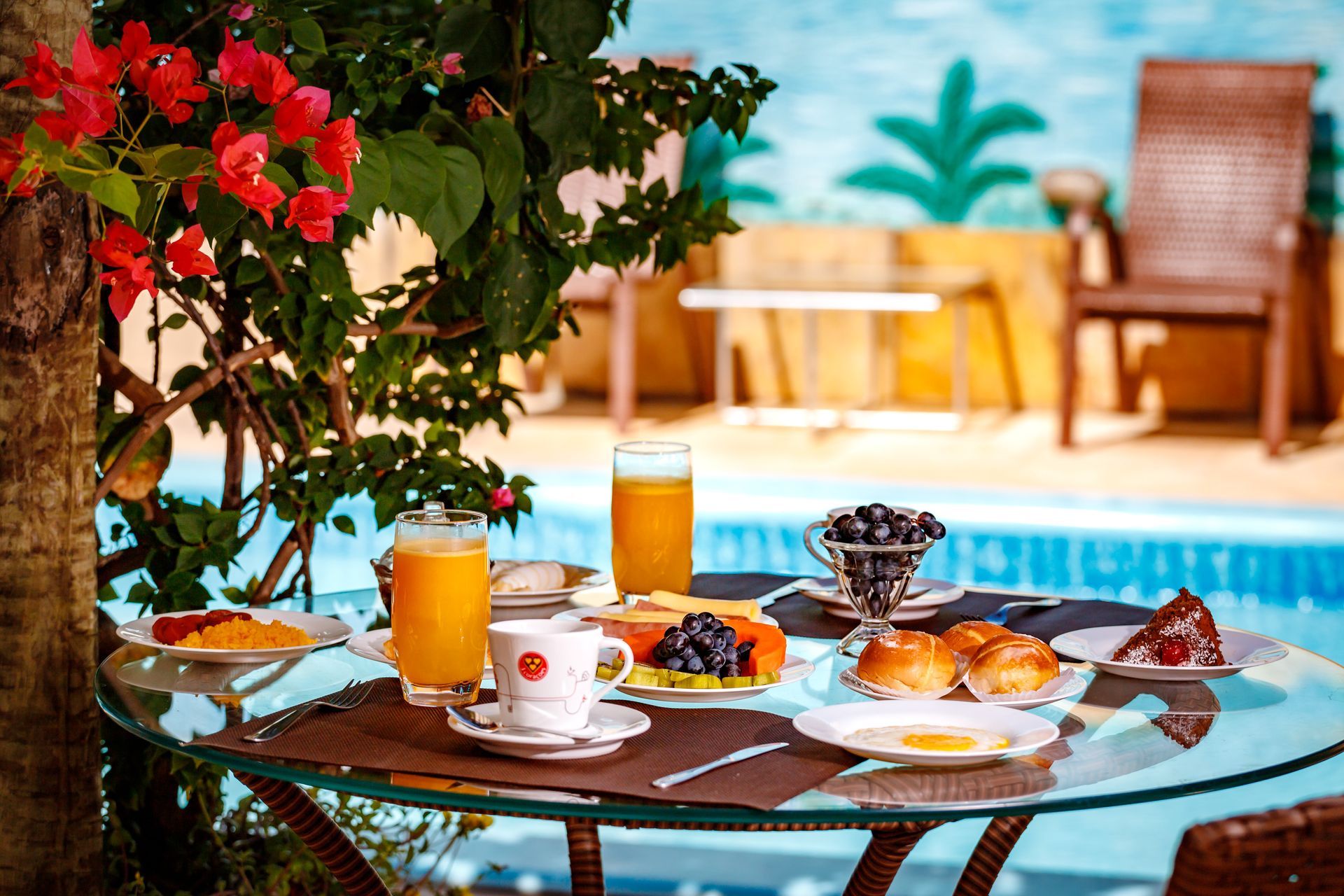 Uma mesa com pratos de comidas e bebidas em frente a uma piscina.