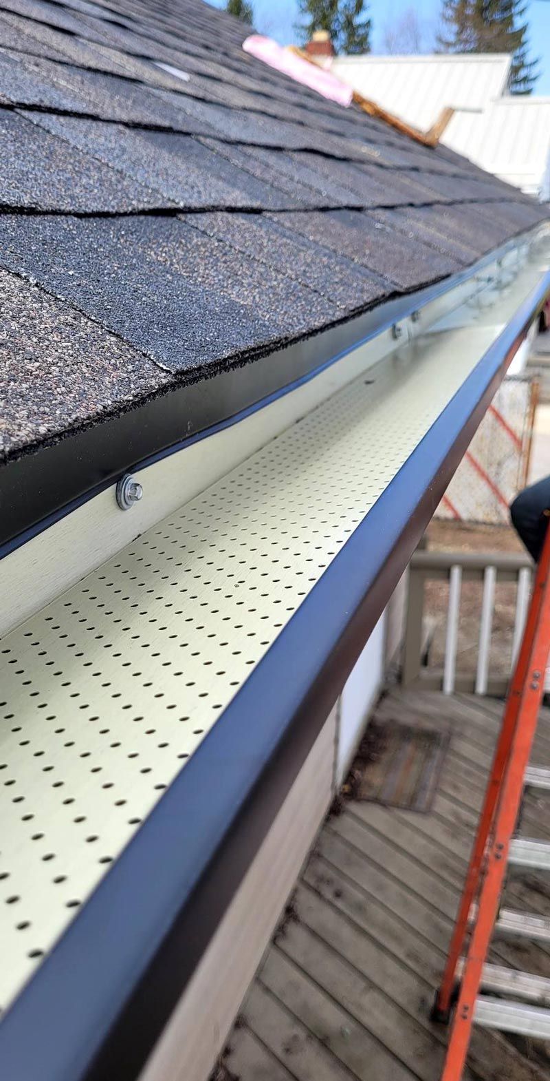 A person is standing on a ladder next to a gutter on the side of a house.
