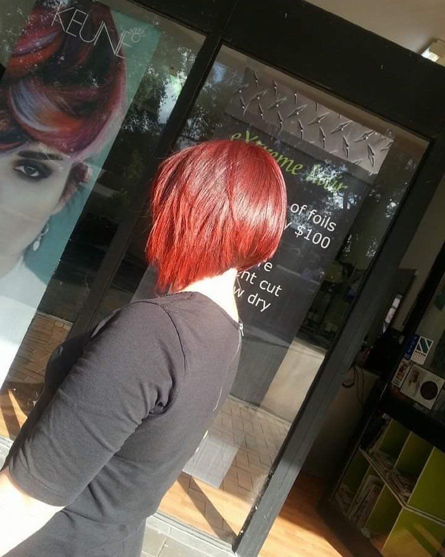 A Woman With Red Hair is Standing in Front of a Keune Sign — Style Haircuts in Gosford, NSW