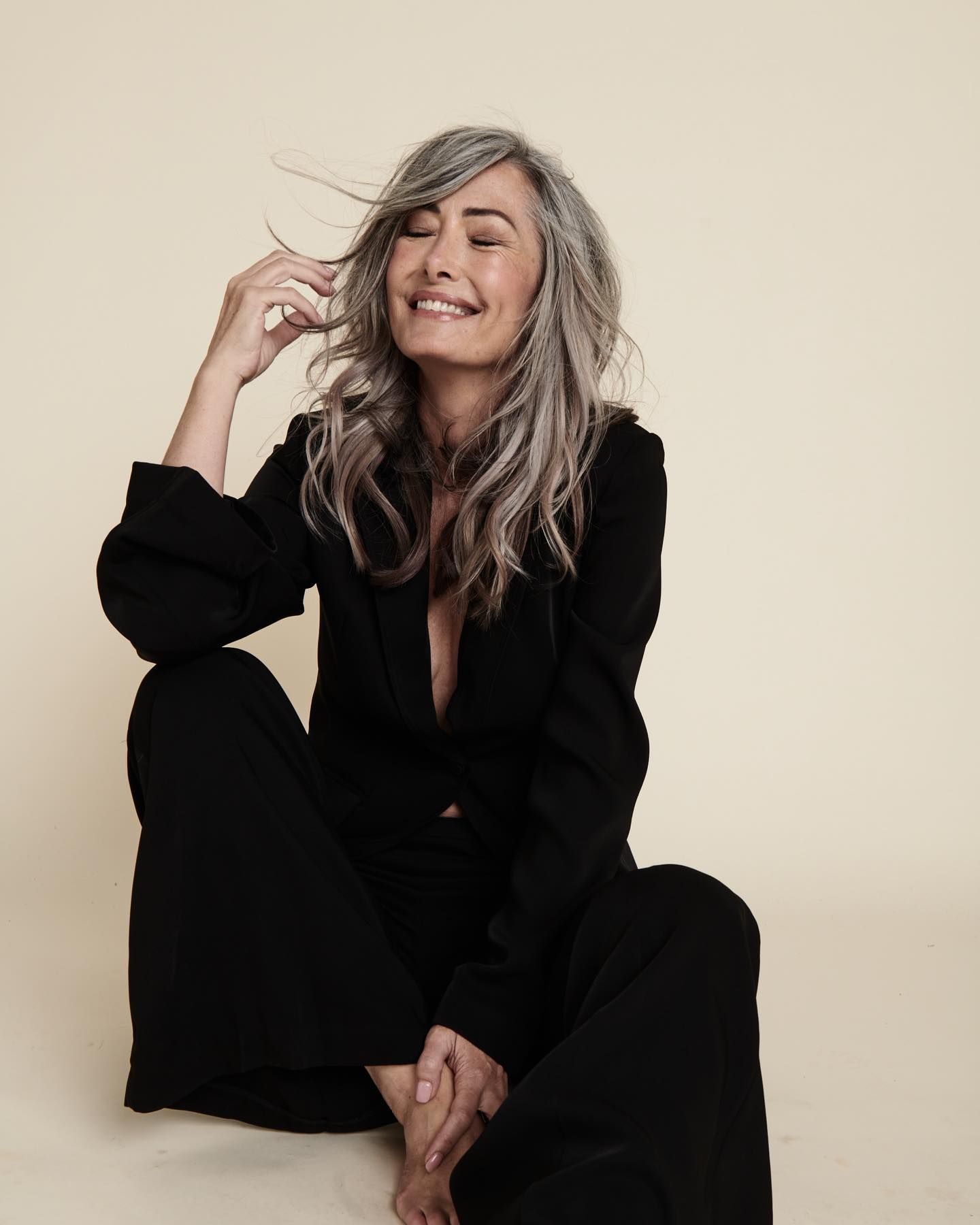 A Woman With Gray Hair is Sitting on the Floor and Smiling — Quality Hair Extensions in Gosford, NSW