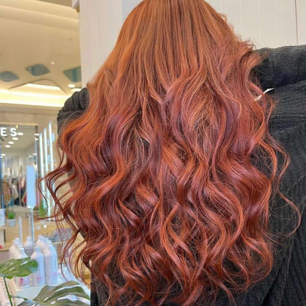 A Woman With Long Red Hair is Standing in Front of a Mirror in a Salon — Experienced Hair Stylist in Gosford, NSW