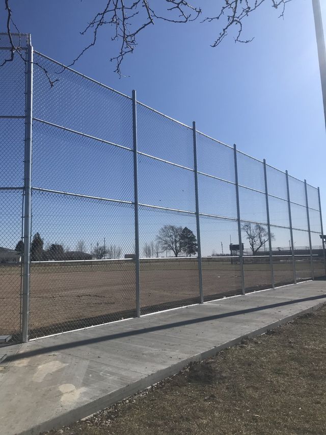 A chain link fence surrounds a baseball field on a sunny day.