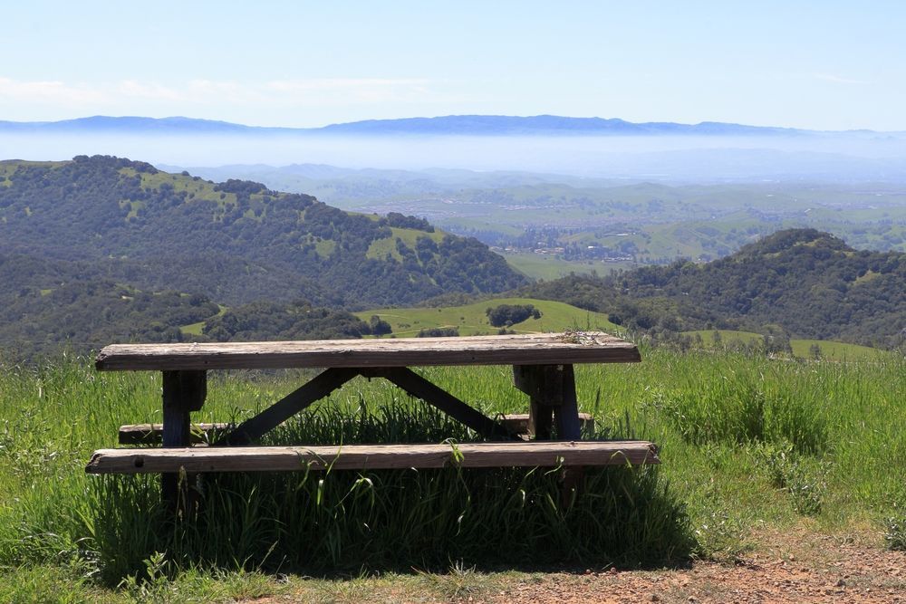 Picnic table on a hillside overlooking a valley with rolling hills, shrouded in a morning haze.