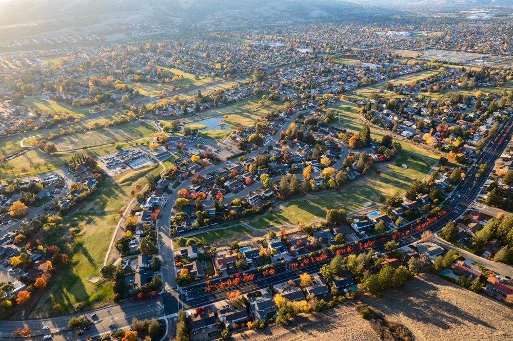 Aerial view of a suburban neighborhood with houses, roads, and a golf course under a sunny sky.