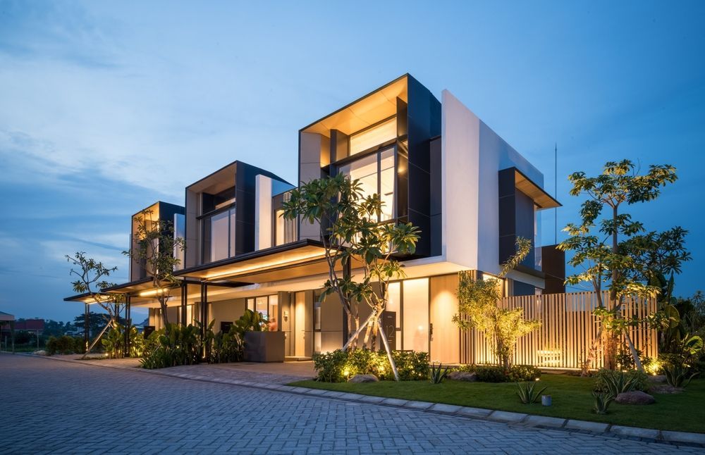 Modern two-story house with illuminated exterior, large windows, and a paved driveway.
