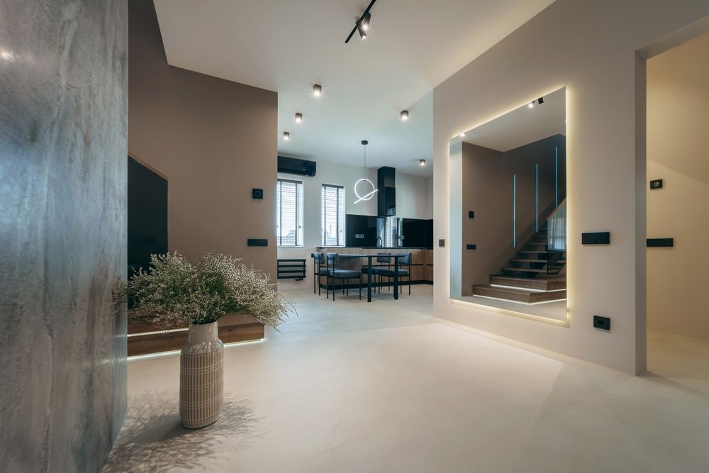 Modern open-plan interior with kitchen, dining area, and staircase. Neutral color palette, large mirror, and decorative vase.