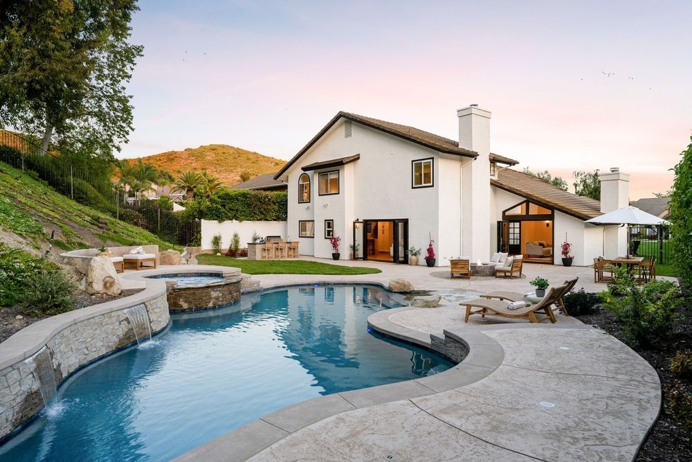 White house with pool, patio, and mountain backdrop at dusk.