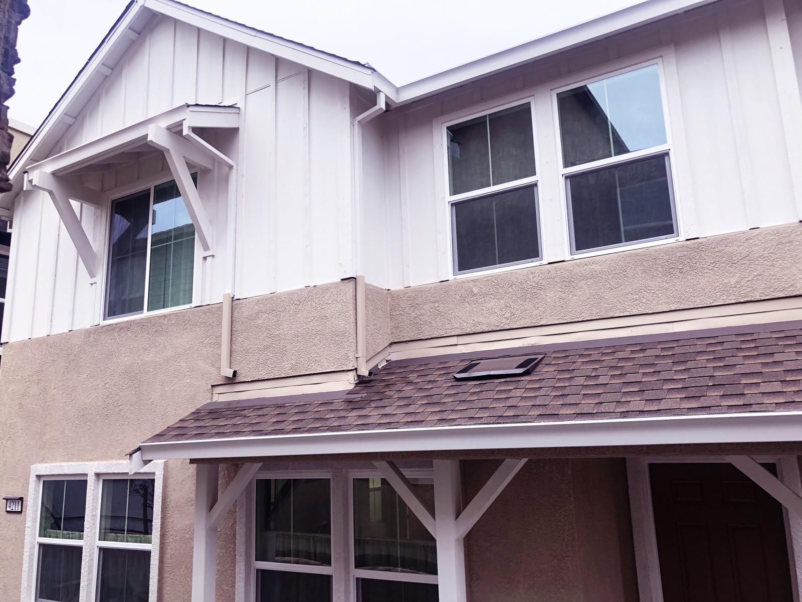 Two-story house with white siding and brown roof. Several windows, including a window awning, are visible.