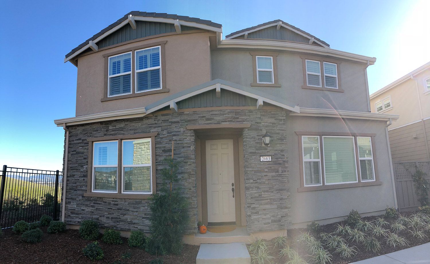 Two-story house with stone facade, tan stucco, and multiple windows against a clear blue sky.