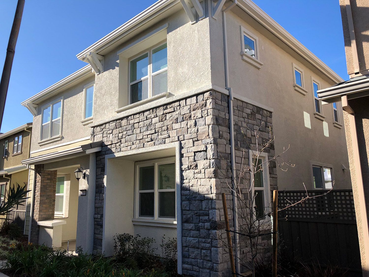Two-story house with stone veneer accents, stucco exterior, multiple windows, blue sky.