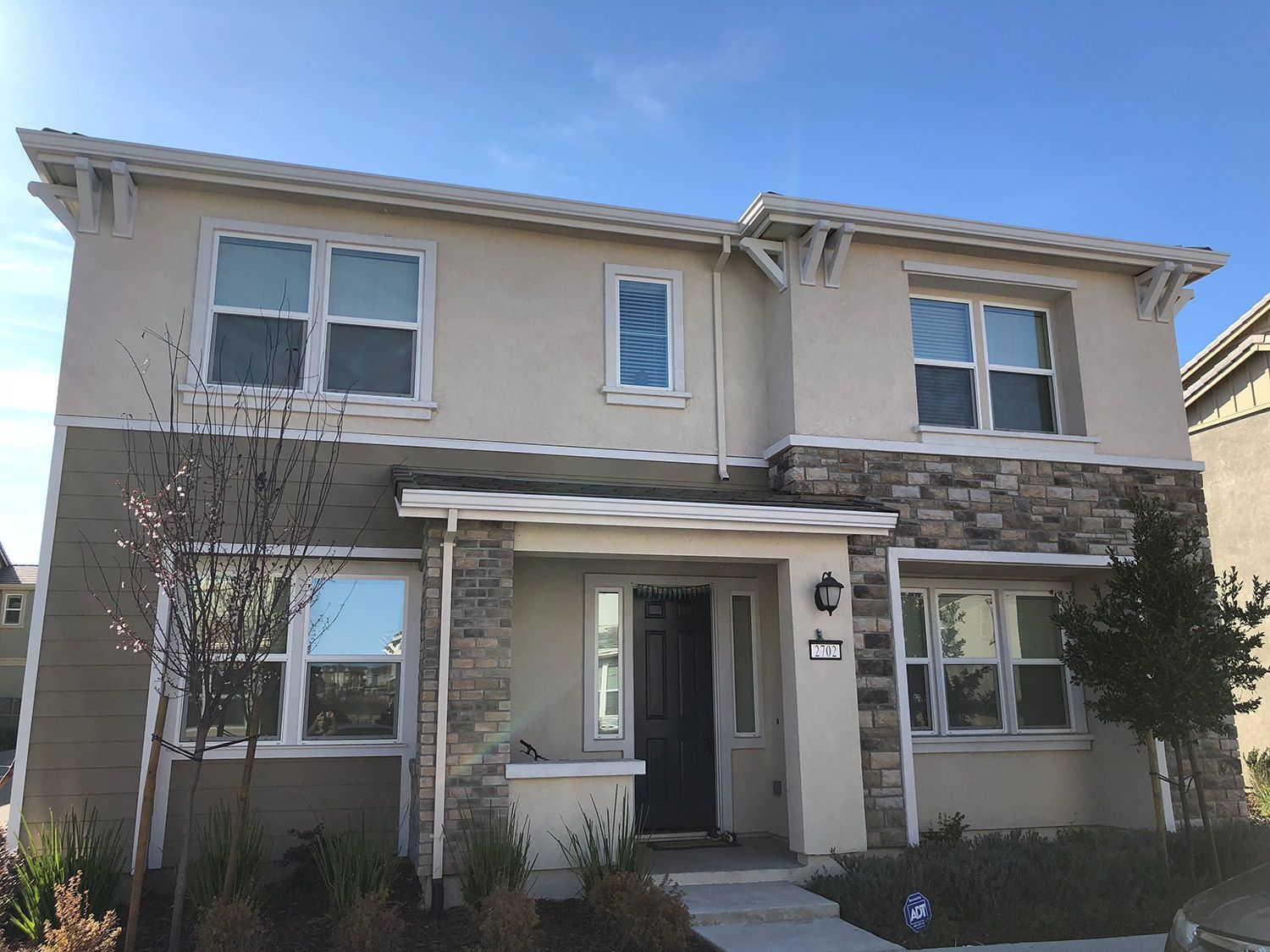 Two-story house with tan stucco and stone facade, multiple windows, blue sky.