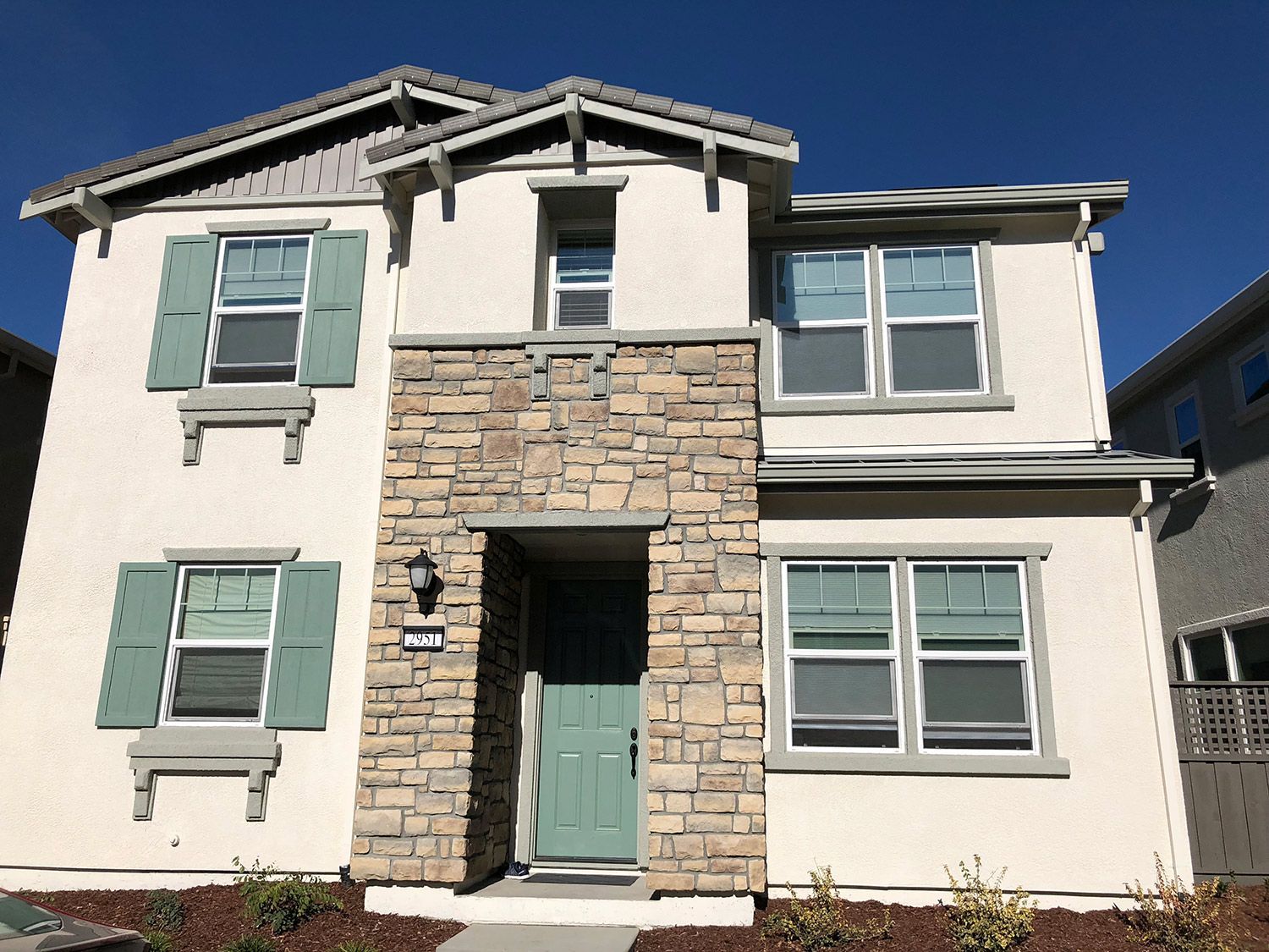 Two-story house with stone facade, light blue door and shutters, beige walls, and blue sky.