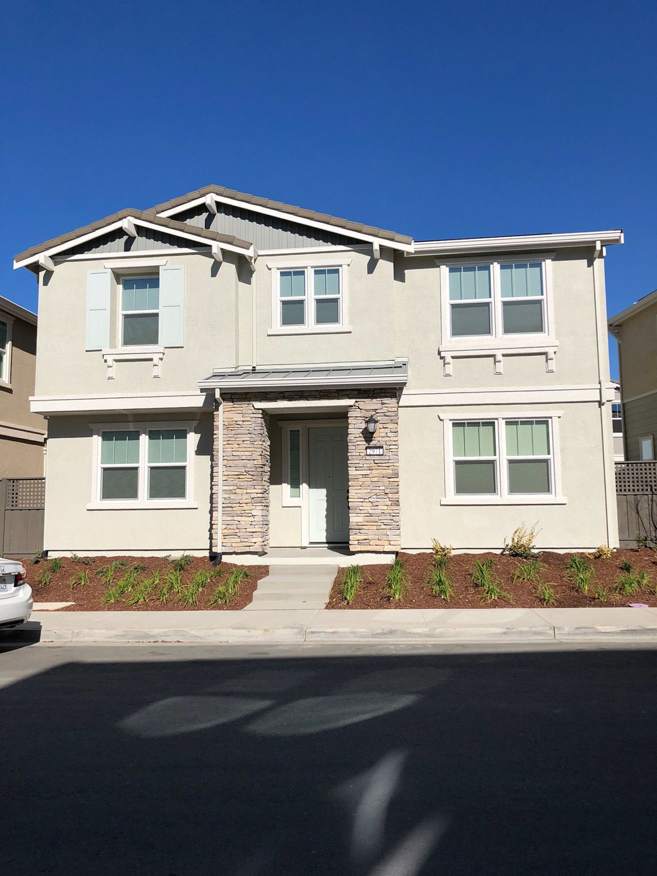 Two-story house with beige stucco, white trim, stone accents, and a blue sky.