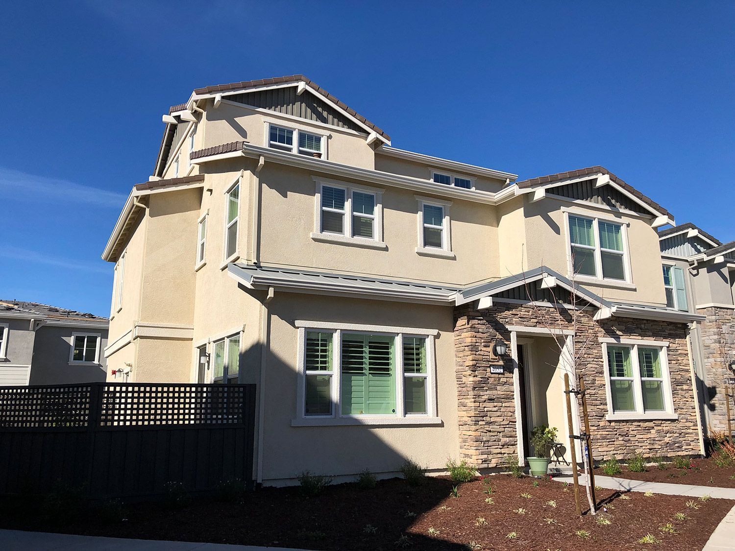 Multi-story beige house with stone accents, windows, and a dark fence.