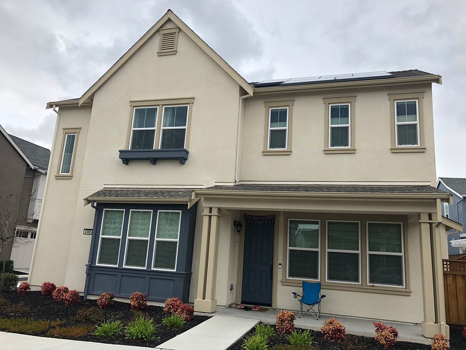 Two-story beige house with dark blue trim and front porch, cloudy day.