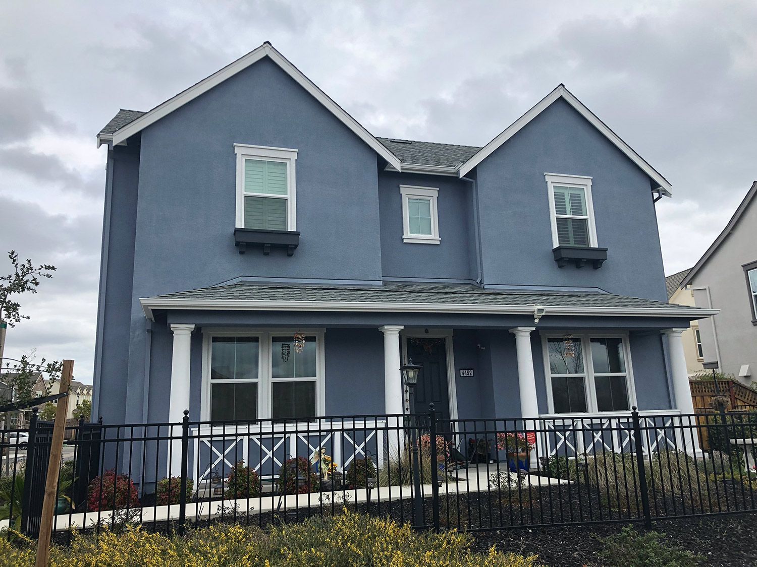 Blue two-story house with white trim, porch, and black fence against a cloudy sky.