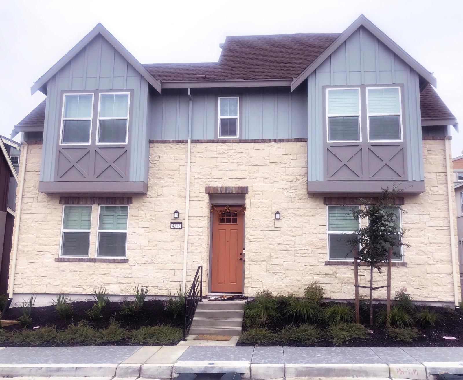 Two-story townhouse with beige stone facade and blue gable accents, brown door and roof.