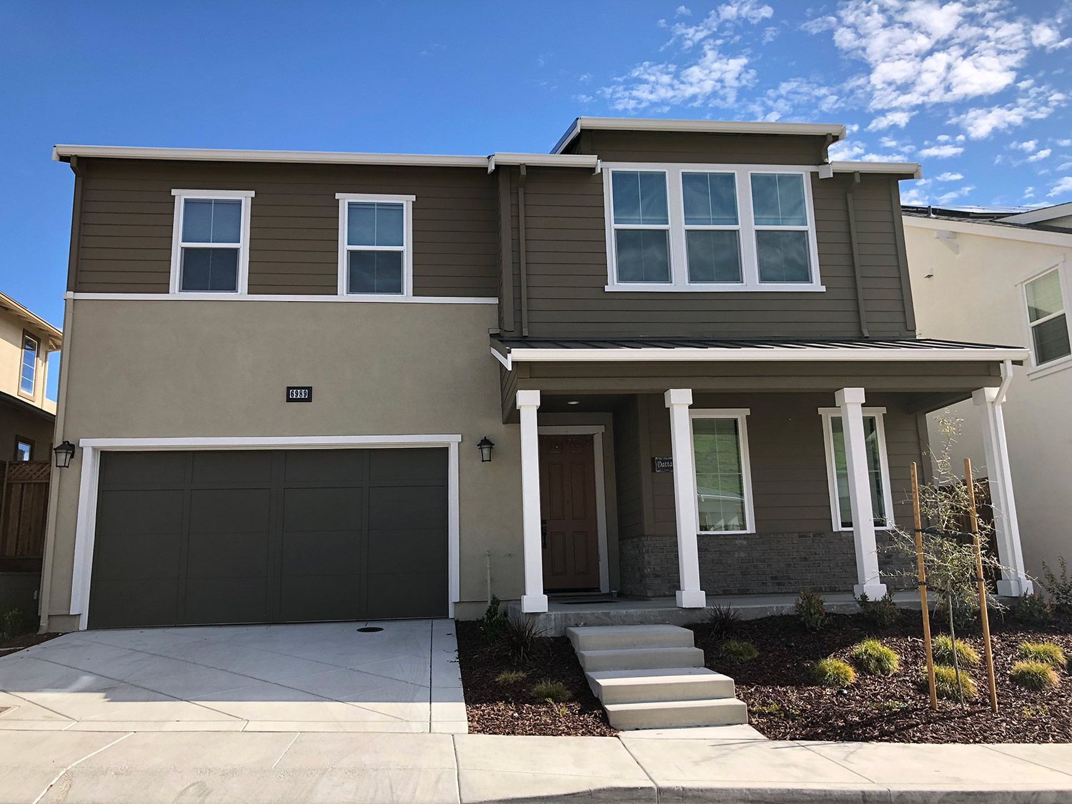 Two-story house with tan and brown siding, a gray garage door, and a small front porch.